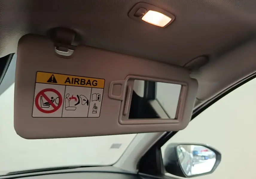 Détail intérieur du pare-soleil côté conducteur avec miroir et avertissement airbag, rétroviseur extérieur visible.