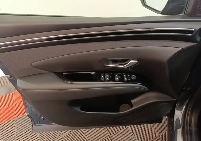 Vue côté gauche de la porte avant d’un Hyundai Tucson bleu, avec commandes de vitres et poignée argentée.