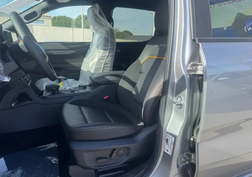 Vue côté gauche intérieur du Ford Ranger gris 2025, siège avant Wildtrak avec surpiqûres orange et accoudoir central.