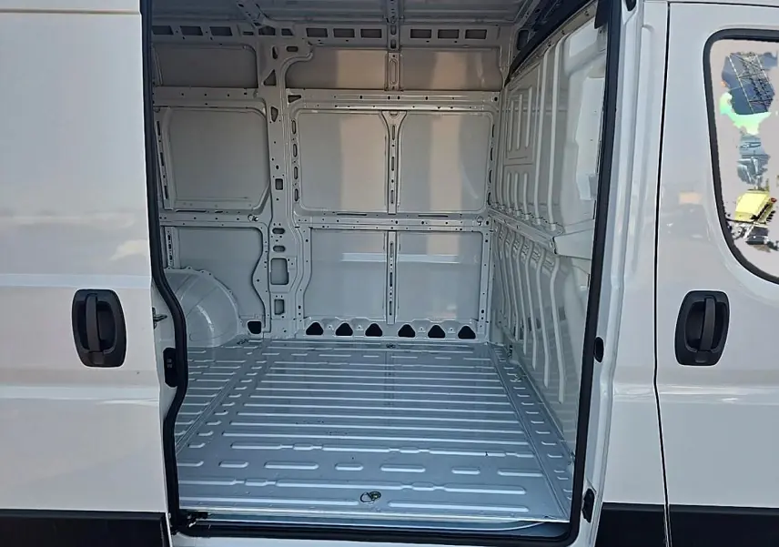 Vue intérieure du fourgon blanc Peugeot Boxer L2h2 2026, montrant l’espace de chargement vide par la porte latérale ouverte.