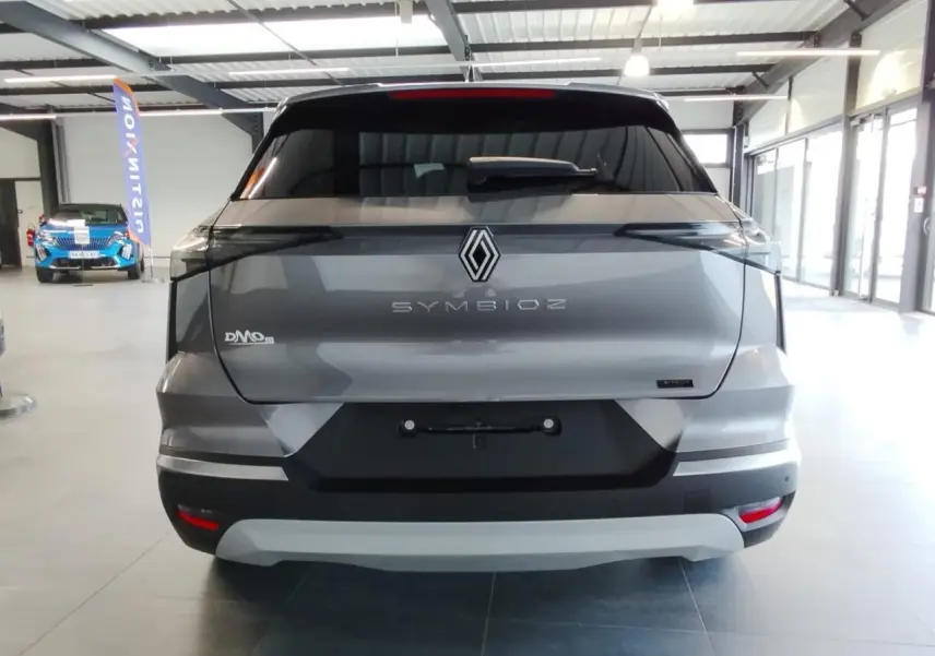 Vue arrière d’un Renault Symbioz gris Cassiopée avec logo central et feux arrière noirs étirés en intérieur showroom.