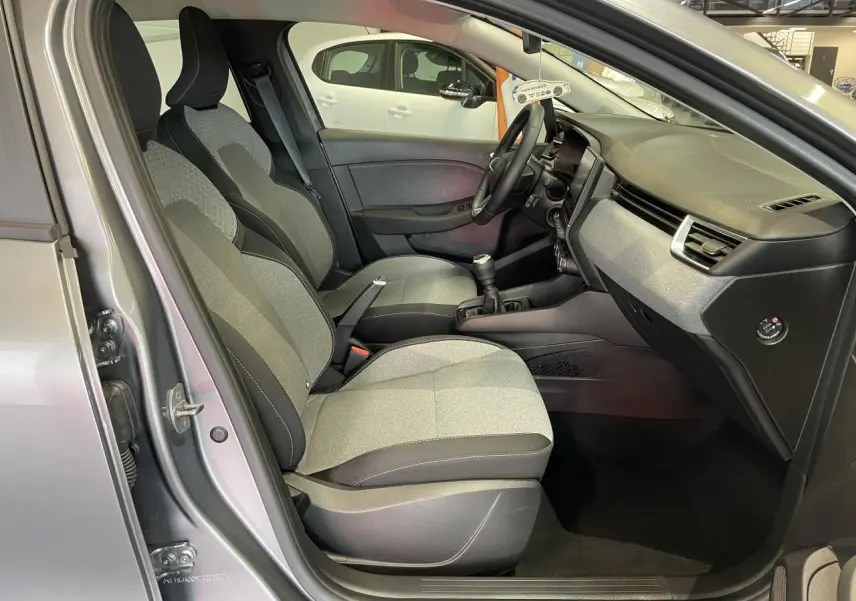 Vue intérieure côté conducteur de la Renault Clio 2024 gris foncé, montrant les sièges tissu gris et la console centrale avec boîte manuelle.