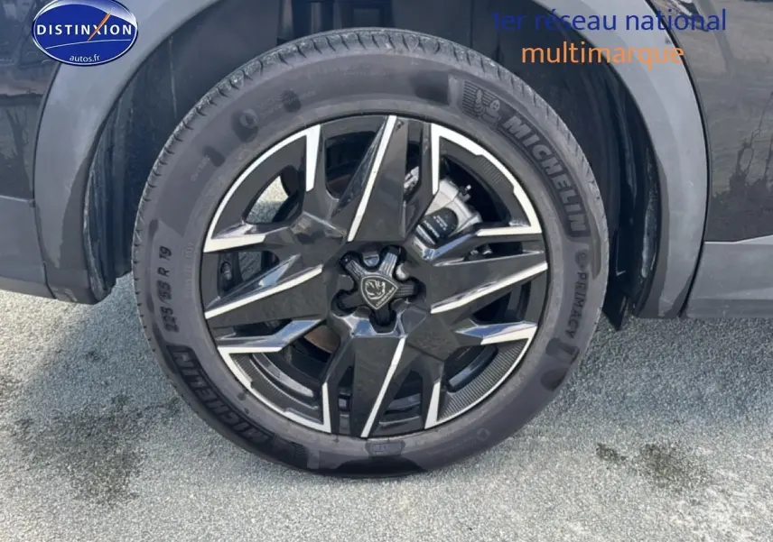 Gros plan sur la roue avant gauche noire d’un Peugeot 5008 Hybrid 145 allure e-dcs6 avec jante alu distinctive.
