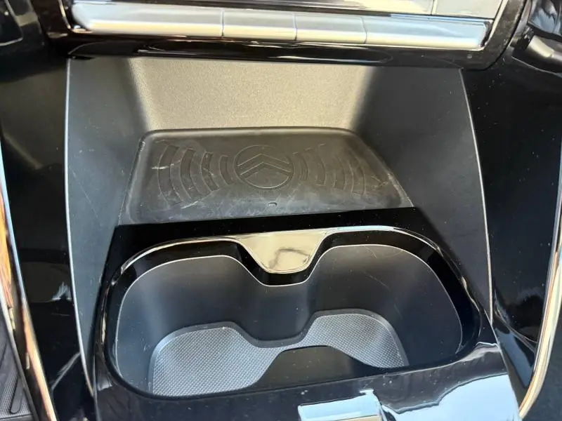 Détail de la console centrale noire avec porte-gobelets et zone de charge sans fil siglée Citroën dans une C3 électrique 2025.