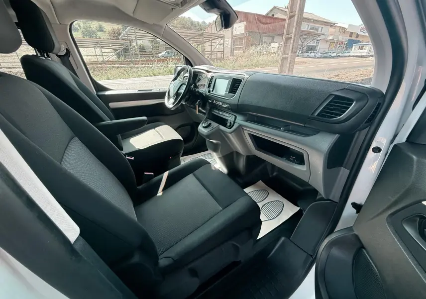 Vue intérieure côté conducteur du Peugeot Expert cabine approfondie blanc, montrant les sièges tissu gris noir et le tableau de bord moderne.