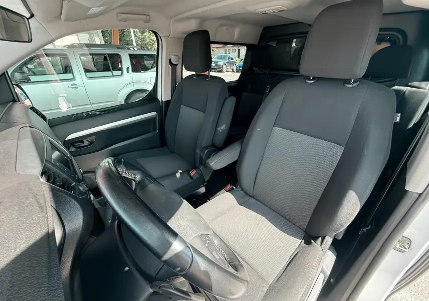 Vue intérieure côté conducteur du Peugeot Expert cabine approfondie blanc, sièges tissu gris noir et volant cuir.