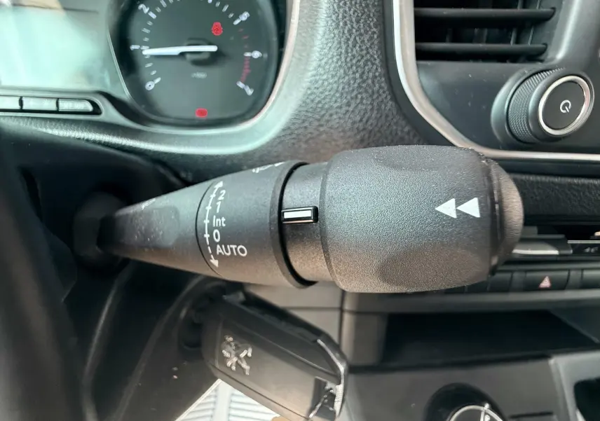 Gros plan sur la commande d’essuie-glace à gauche du volant dans l’habitacle gris noir du Peugeot Expert cabine approfondie blanc.