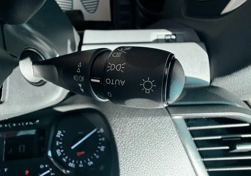 Gros plan sur la commande des phares noire à gauche du volant dans l’habitacle gris du Peugeot Expert Cabine Approfondie blanc.