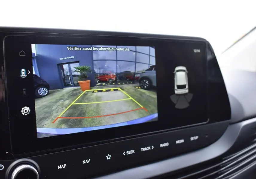 Écran tactile intérieur montrant la caméra de recul d'une Hyundai i20 bleu clair avec aides au stationnement.