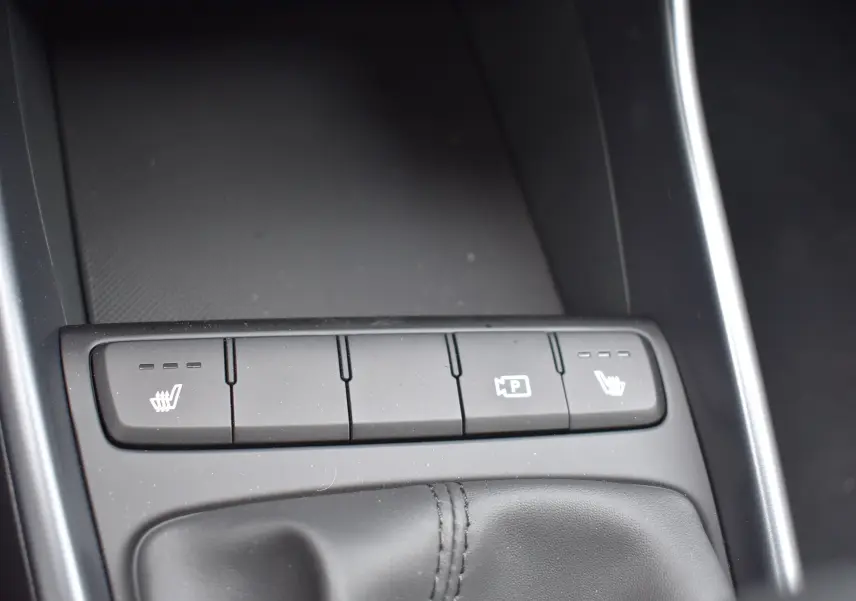 Gros plan sur la console centrale de la Hyundai i20 2025, boutons de sièges chauffants et aide au stationnement visibles.