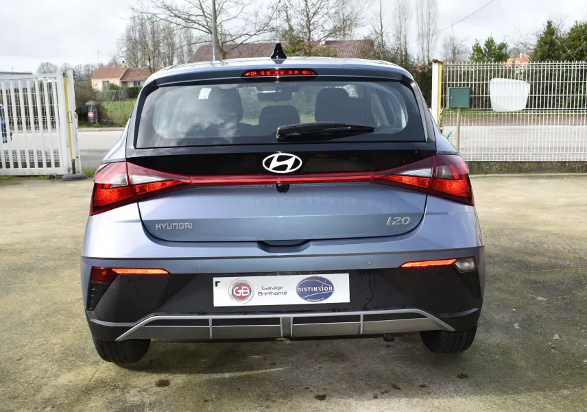 Vue arrière d'une Hyundai i20 bleu clair 2025 avec feux arrière allumés et spoiler de toit visible.