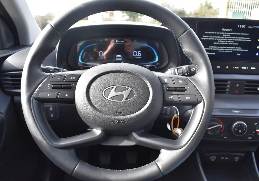 Vue rapprochée du volant en cuir noir de la Hyundai i20 2025 avec commandes multifonctions et tableau de bord digital.
