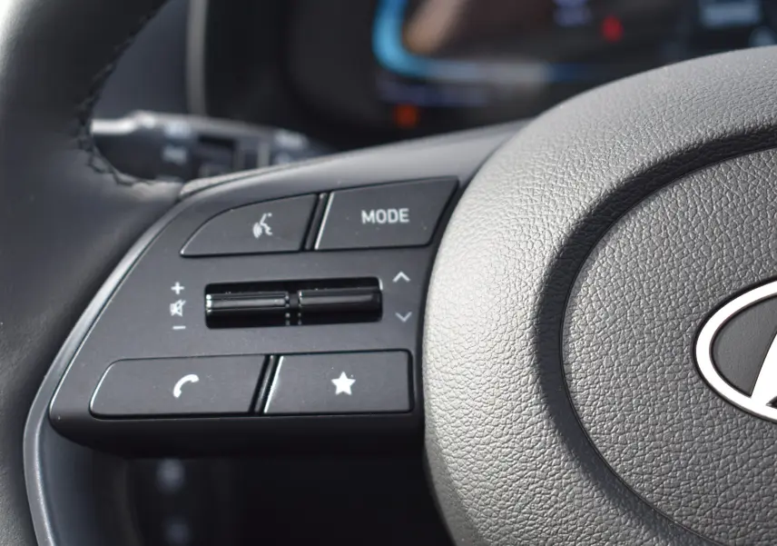 Gros plan sur les commandes audio au volant d'une Hyundai i20 2025, volant en cuir gris foncé.