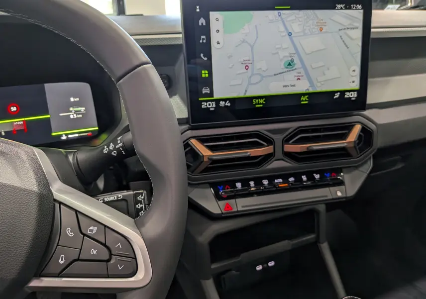 Vue intérieure centrée sur le tableau de bord et l’écran tactile du Dacia Bigster Mild Hybrid bleu indigo, avec volant partiel visible.