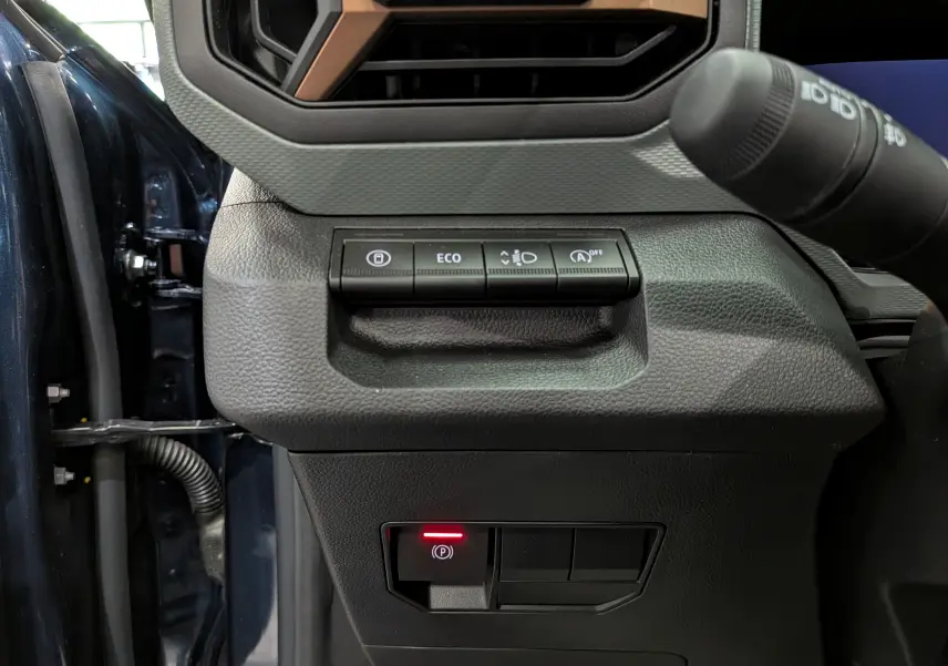 Gros plan sur les commandes à gauche du volant du Dacia Bigster bleu indigo, avec bouton de frein à main électronique allumé.