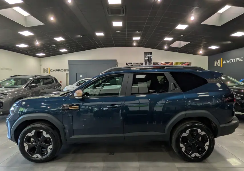 Vue de profil côté gauche du Dacia Bigster bleu indigo, avec jantes noires et toit noir en concession.