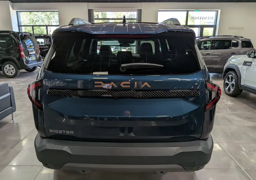 Vue arrière du Dacia Bigster bleu indigo en showroom, avec logo Dacia lumineux et feux arrière modernes.