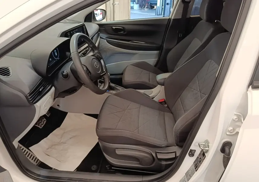 Vue intérieure côté conducteur de la Hyundai Bayon blanche 2024, montrant sièges tissu gris et tableau de bord digital.