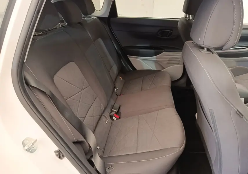 Vue intérieure côté gauche montrant la banquette arrière grise du Hyundai Bayon blanc 2024 avec ceinture de sécurité.