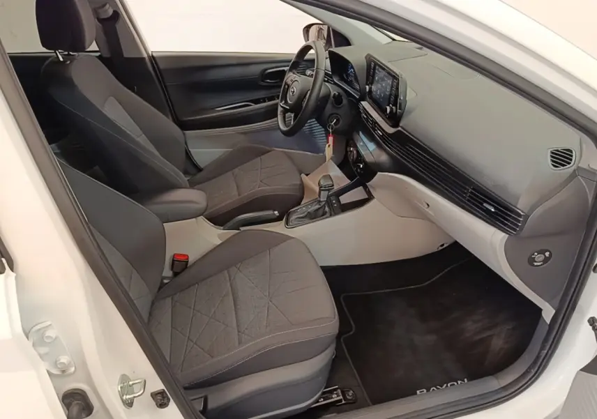 Vue intérieure côté conducteur de la Hyundai Bayon blanche 2024, montrant sièges noirs et tableau de bord moderne avec écran tactile.
