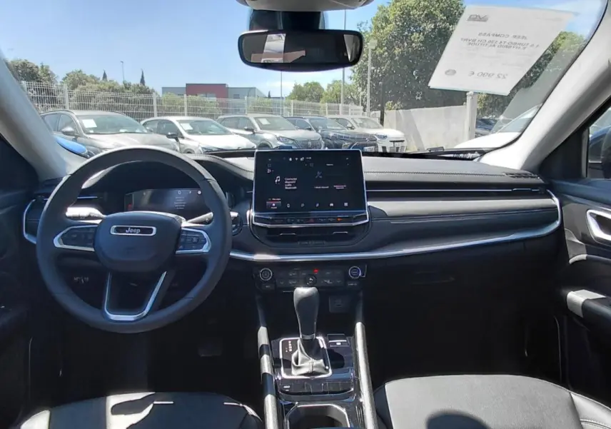 Vue intérieure avant du Jeep Compass 2025 avec tableau de bord noir, écran tactile et volant multifonction.