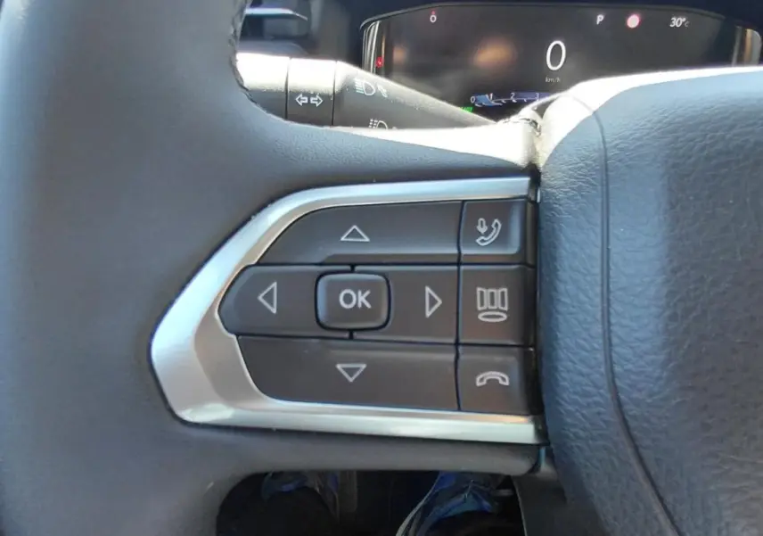 Gros plan sur les commandes gauche du volant en cuir noir du Jeep Compass bleu 2025, affichage numérique en arrière-plan.