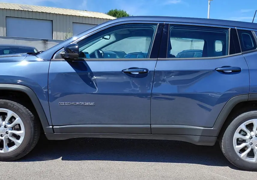 Vue de profil côté gauche d’un Jeep Compass bleu 2025 avec jantes alliage 18 pouces et logo visible sur la porte.