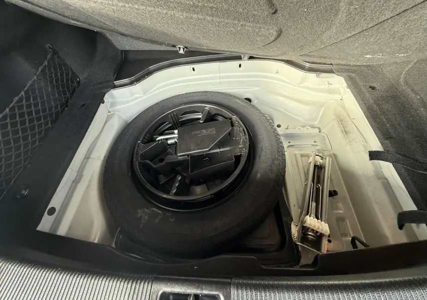 Vue plongeante sur la roue de secours et le cric dans le coffre d'une Mercedes Classe E 250 Coupé gris.