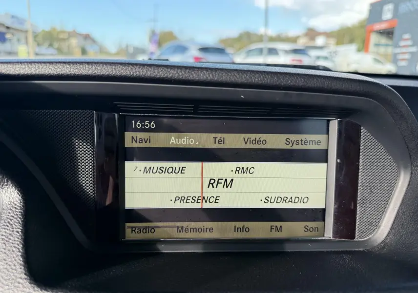 Écran central du système multimédia d'une Mercedes Classe E 250 Coupé gris, affichant les stations radio FM.