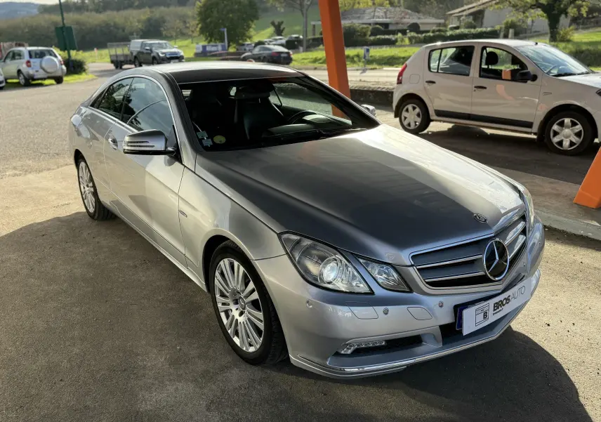 Mercedes Classe E 250 Coupé gris vue 3/4 avant droit, avec jantes alliage et calandre chromée sous lumière naturelle.