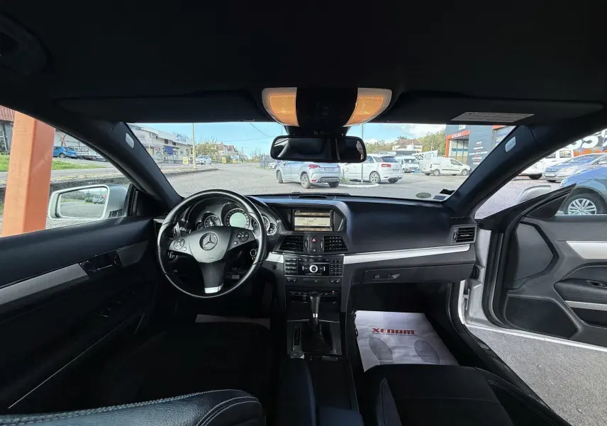 Vue intérieure avant de la Mercedes Classe E 250 Coupe gris, avec tableau de bord noir et volant multifonction.