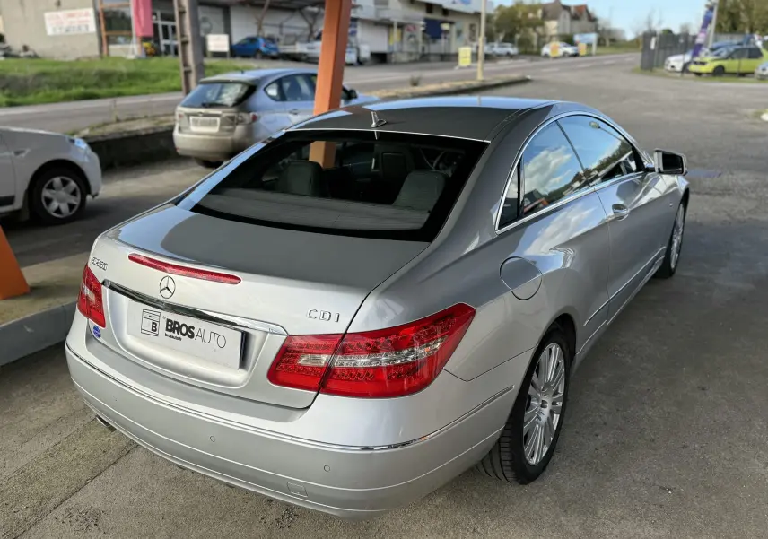Vue 3/4 arrière droite d'une Mercedes Classe E 250 CDI gris métallisé stationnée sous abri avec jantes alliage.