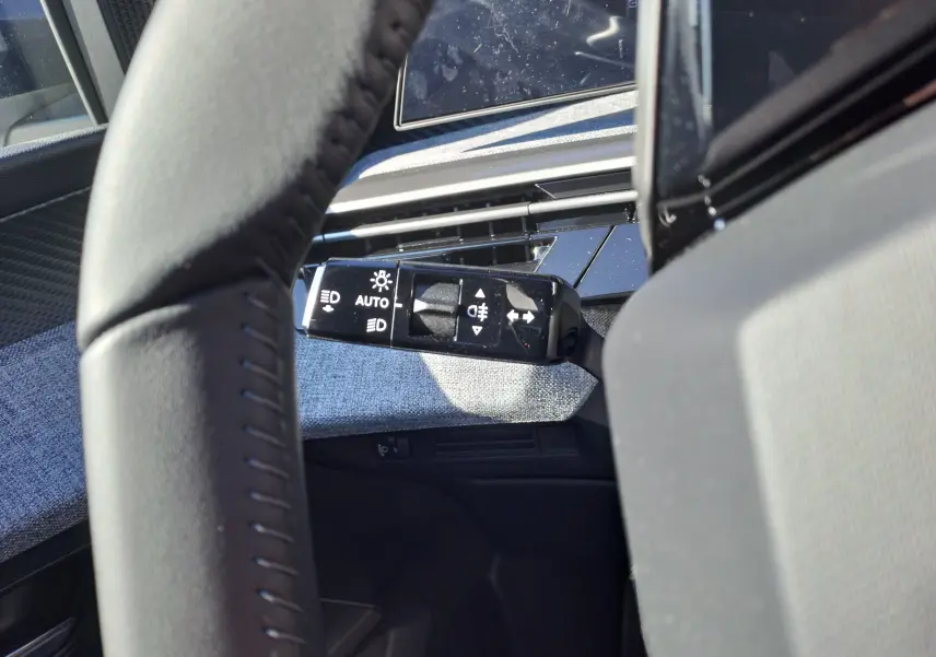 Gros plan sur la commande des phares à gauche du volant dans l'habitacle gris du Peugeot 3008 2024.