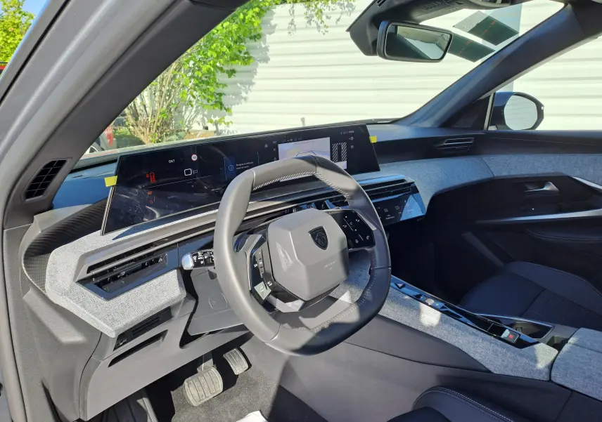 Vue intérieure côté conducteur du Peugeot 3008 gris Artense 2024, mettant en valeur le tableau de bord numérique et le volant compact.
