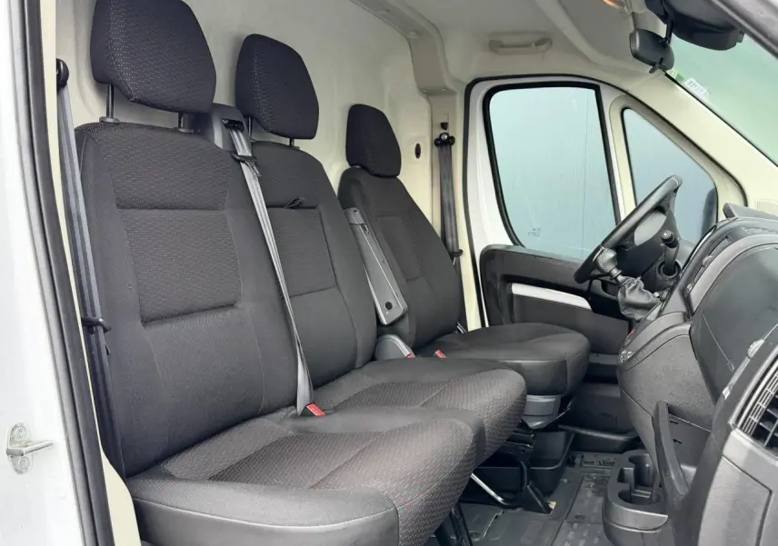 Vue intérieure côté conducteur de l'Opel Movano Fourgon blanc 2024, montrant les sièges avant en tissu noir et le tableau de bord.