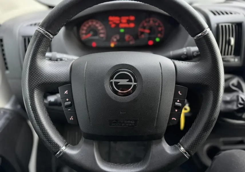 Vue rapprochée du volant en cuir noir de l'Opel Movano Fourgon 2024 avec tableau de bord flou en arrière-plan.