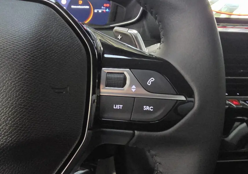 Gros plan sur la partie gauche du volant noir du Peugeot 208 1.2i Hybrid avec commandes multimédia intégrées.