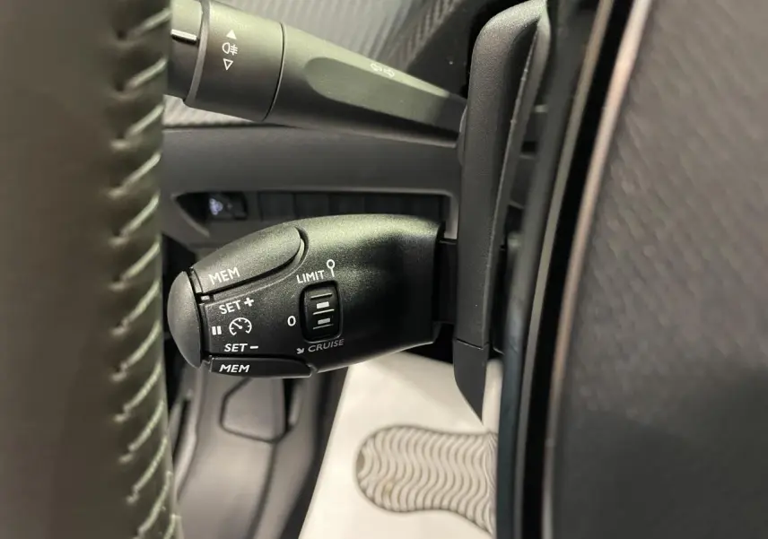 Gros plan sur la commande de régulateur de vitesse noire à gauche du volant de la Peugeot 208 2025.
