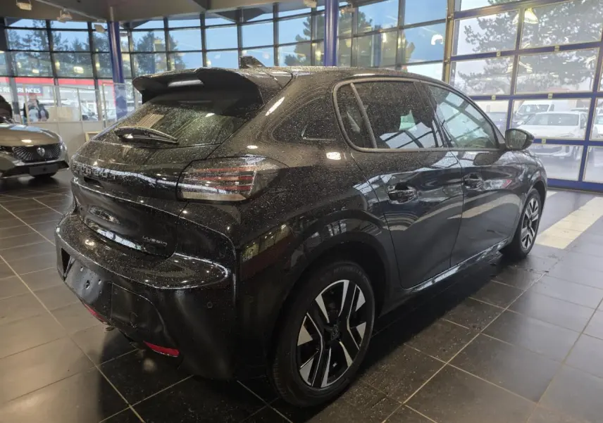 Peugeot 208 hybride noir métallisé vue 3/4 arrière droit en intérieur avec jantes alliage bicolores.