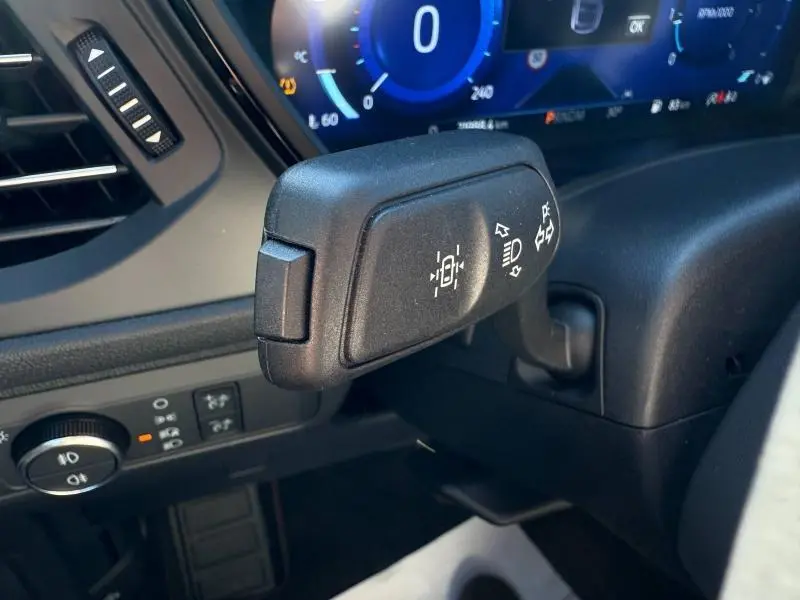 Gros plan sur la commande de feux et régulateur de vitesse du Ford Kuga 2024, intérieur noir avec tableau de bord numérique.