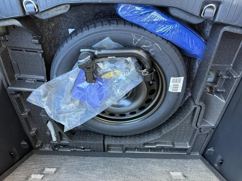 Vue du coffre du Ford Kuga 2024 montrant la roue de secours et l'attelage de remorque emballé en plastique.