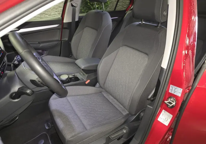 Vue intérieure côté gauche des sièges avant en tissu gris de la Volkswagen Golf VIII rouge métallisée avec accoudoir central.