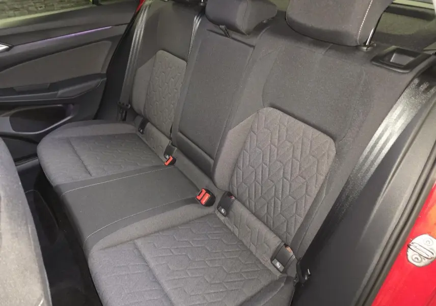 Vue intérieure sur la banquette arrière en tissu gris de la Volkswagen Golf VIII rouge, avec ceintures de sécurité visibles.