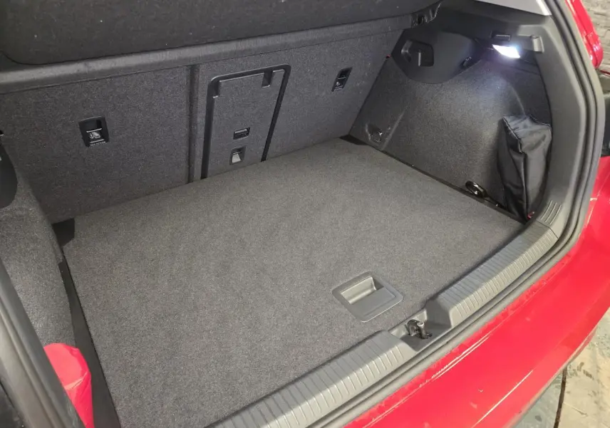 Coffre ouvert vu de dessus d’une Volkswagen Golf VIII rouge, avec tapis gris et éclairage intérieur allumé.
