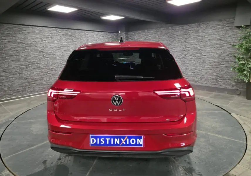 Vue arrière d'une Volkswagen Golf VIII rouge métallisé avec feux arrière LED allumés dans un showroom.