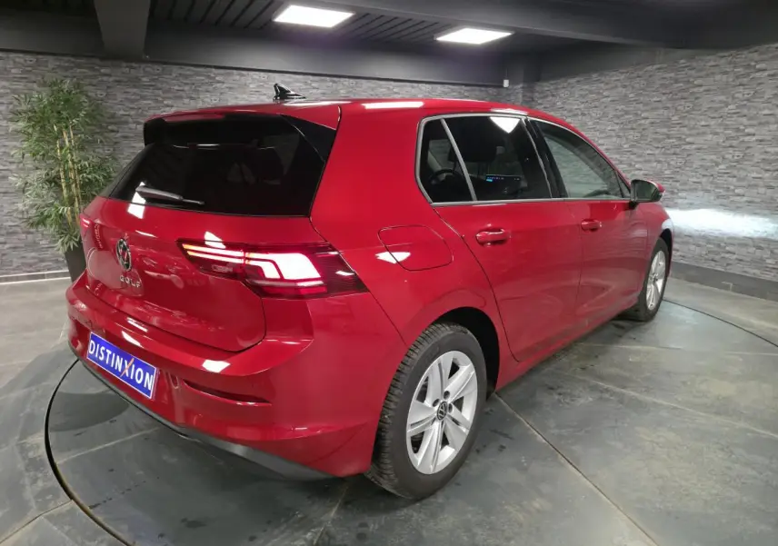 Volkswagen Golf VIII rouge métallisé vue 3/4 arrière droit avec feux arrière LED allumés en intérieur.