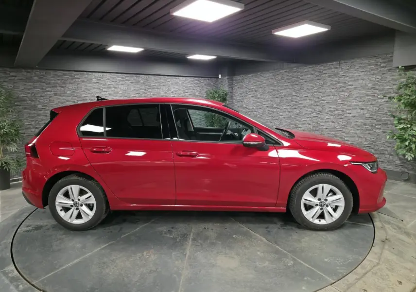 Volkswagen Golf VIII rouge métallisé vue de profil côté gauche en intérieur avec jantes alliage 16 pouces.