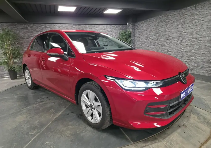 Volkswagen Golf VIII rouge métallisé vue 3/4 avant droit avec phares LED allumés en intérieur.