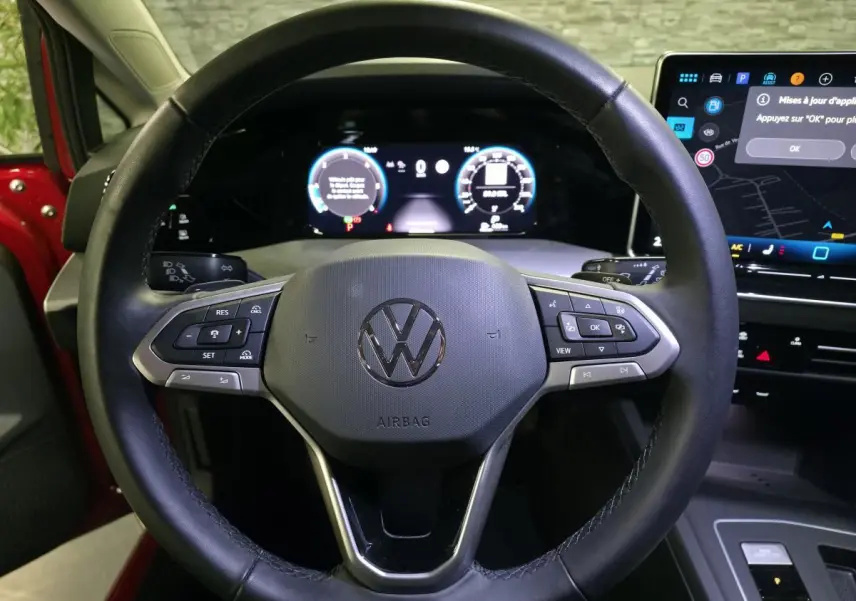 Vue rapprochée du volant noir de la Volkswagen Golf VIII rouge avec tableau de bord digital et écran tactile visible.