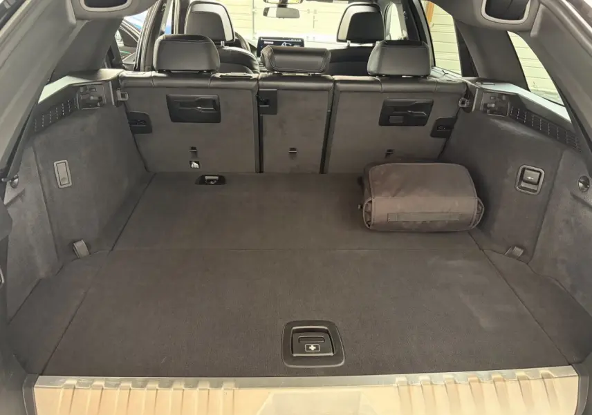 Vue intérieure du coffre spacieux de la BMW Série 5 Touring 530e noir avec banquette arrière rabattue et sac de rangement.